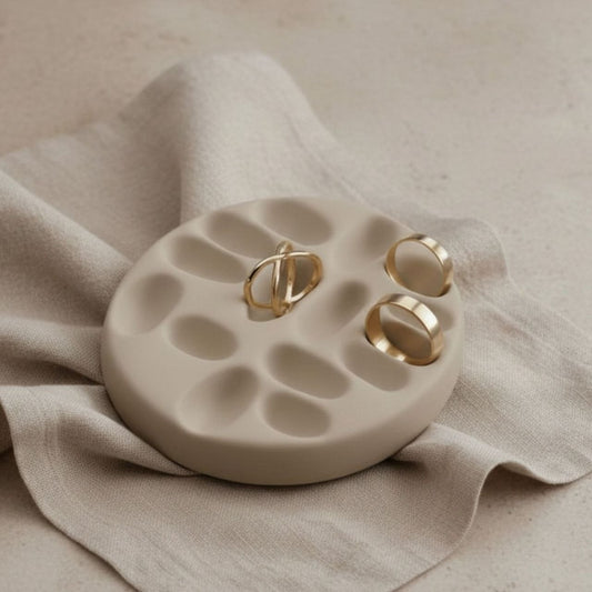 Taupe jewelry tray with gold rings on a beige fabric background