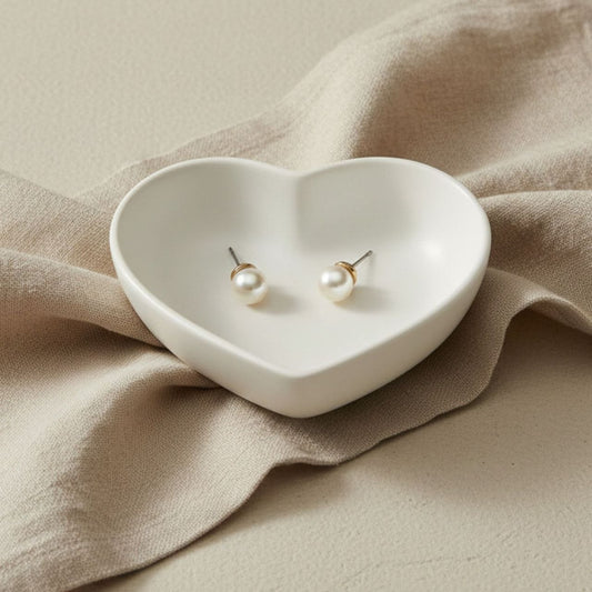 Heart trinket tray in natural finish on a beige background with pearl earrings.