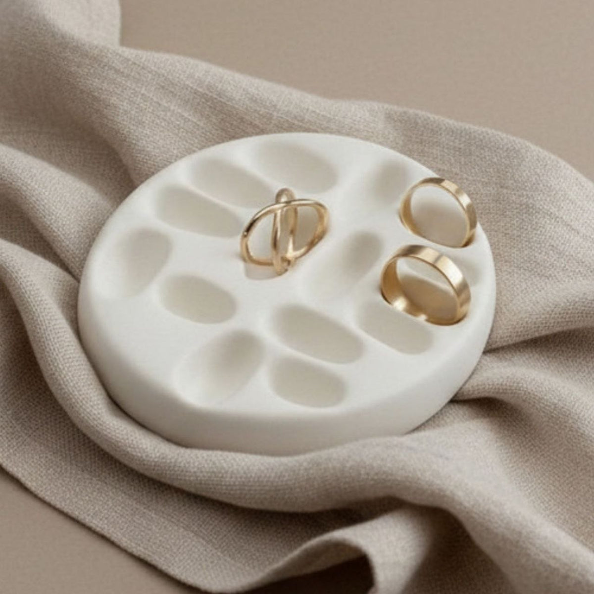 White jewelry tray with gold rings on a beige fabric background
