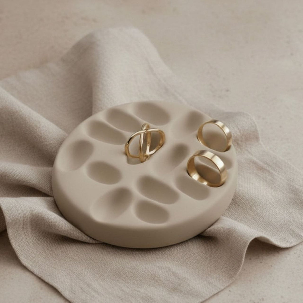 Taupe jewelry tray with gold rings on a beige fabric background