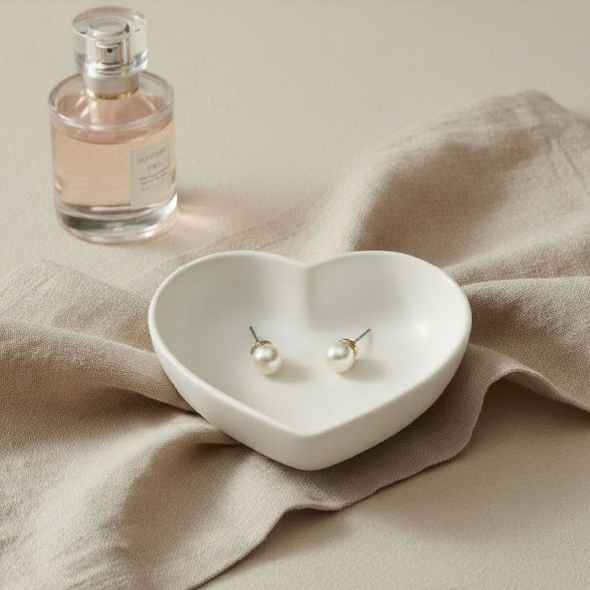 Heart trinket tray in natural finish on a beige background with pearl earrings and a bottle of perfume