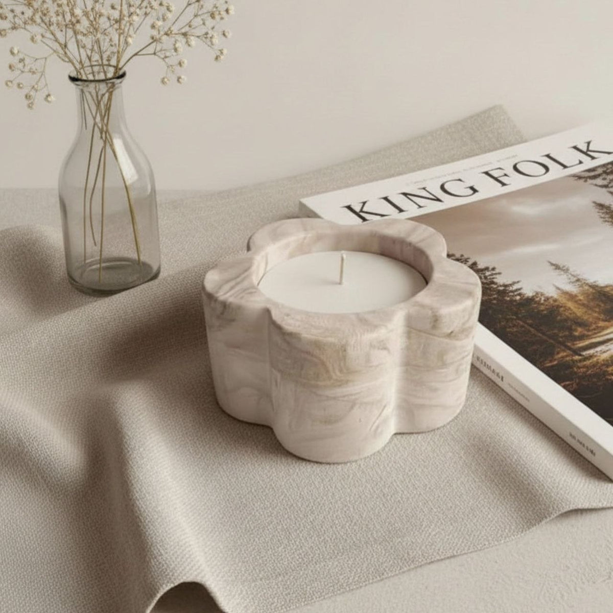 Decorative daisy candle holder on a table with a magazine and vase in the background
