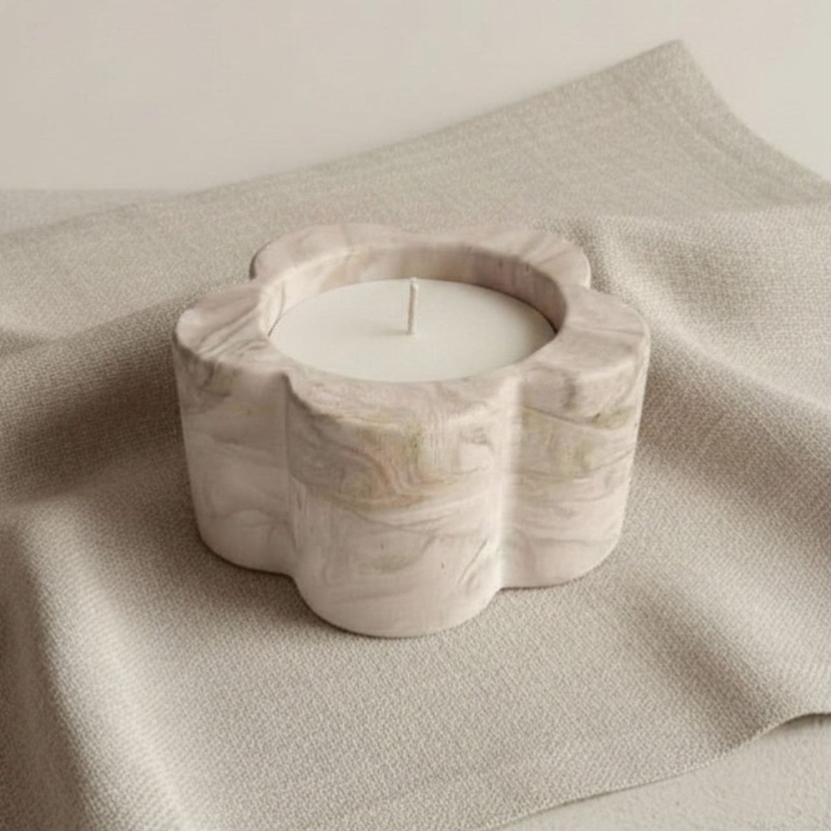 Marble-textured daisy candle holder with a candle on a beige fabric background