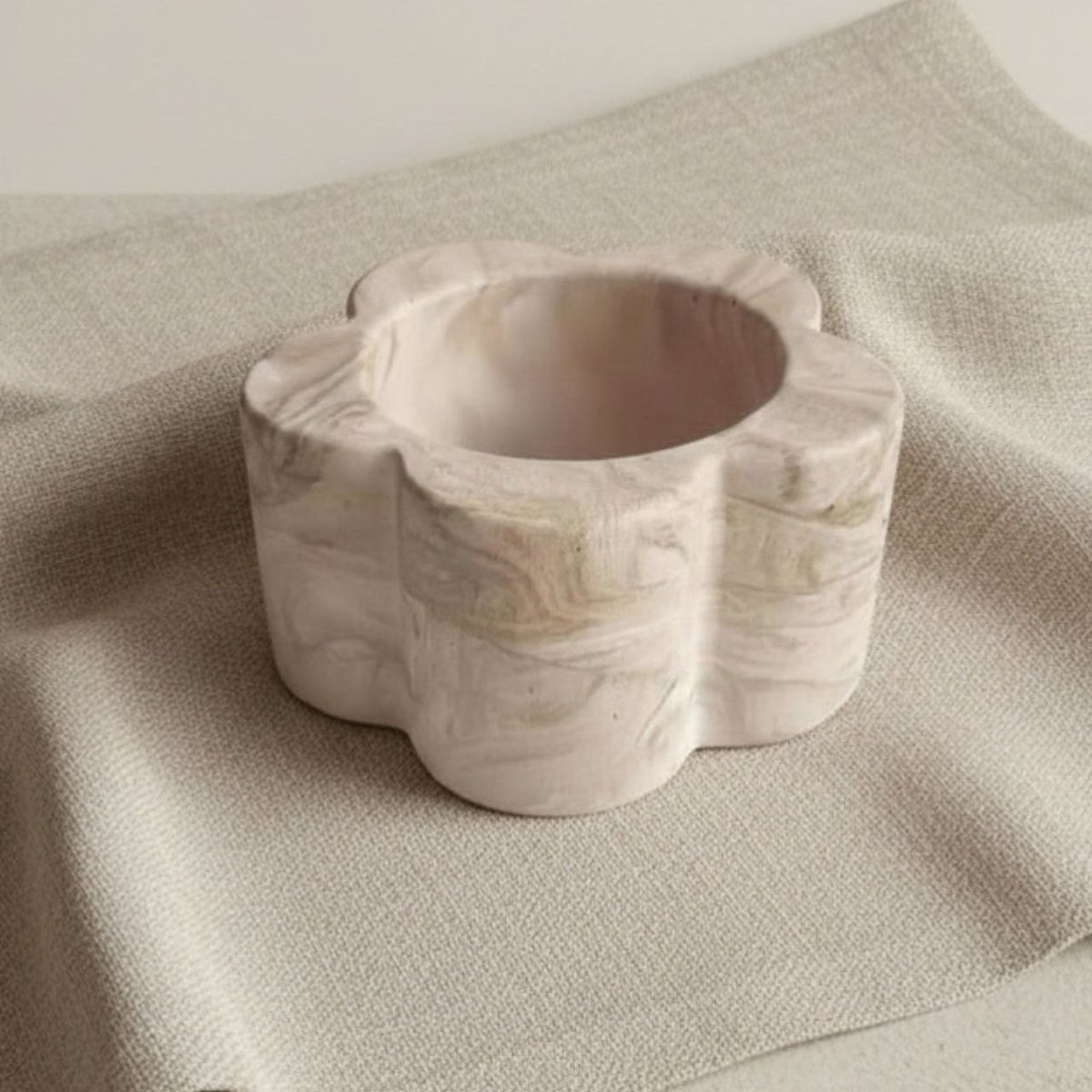 Marble-textured daisy candle holder on a beige fabric background
