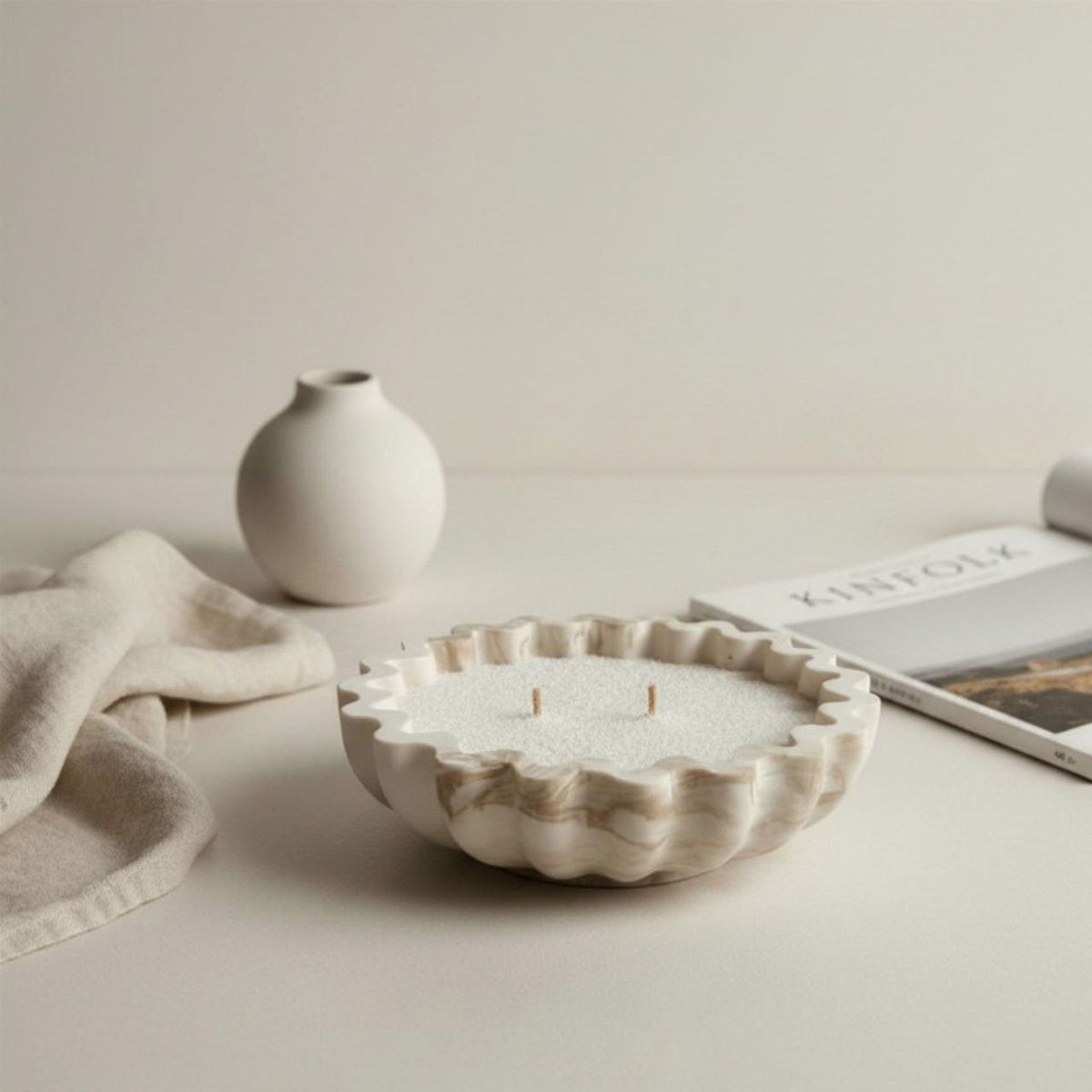 Fluted bowl in a beige marble finish on a table with a vase and a magazine