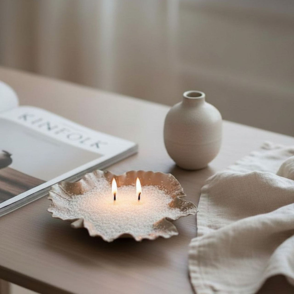 Wax sand candle in a maple leaf dish on a table with a book and vase in the background
