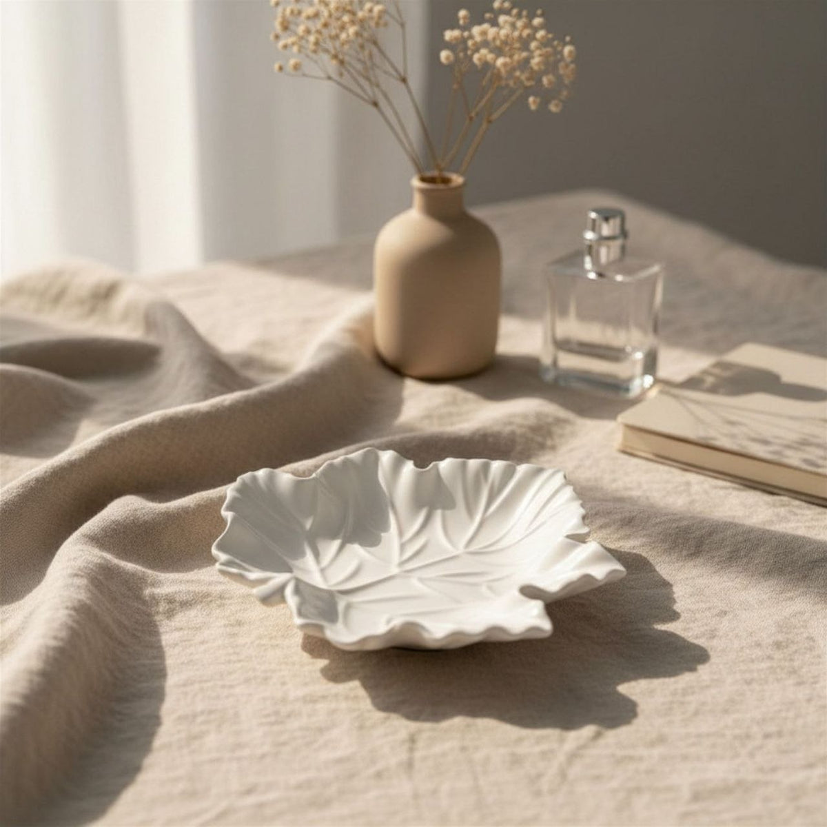 Natural maple leaf tray on a textured surface with a vase and perfume bottle in the background.