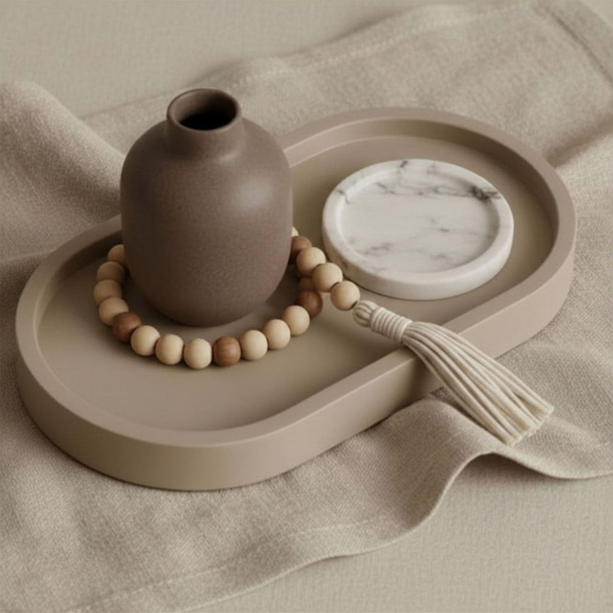 Decorative setting with a brown vase, beads, and cermic disch on a taupe tray.