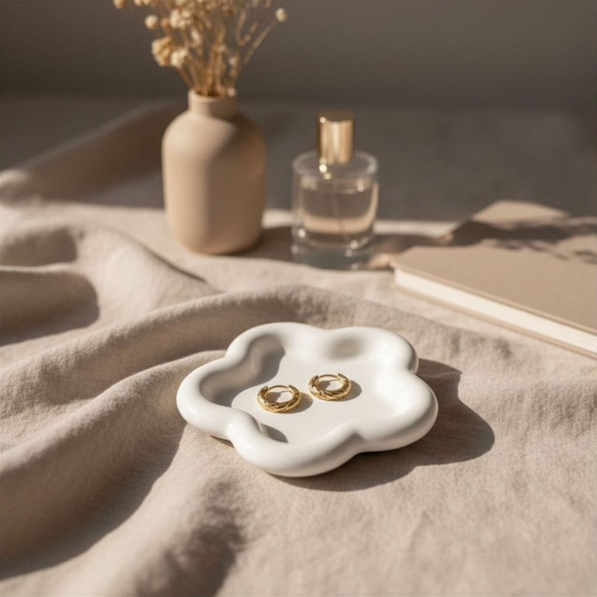 A natural finish flower tray with gold earrings on a beige surface with a vase and perfume bottle in the background.