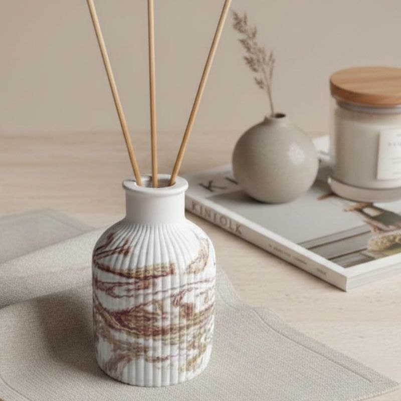 Reed diffuser with a marble finish with a magazine, a vase and a candle jar